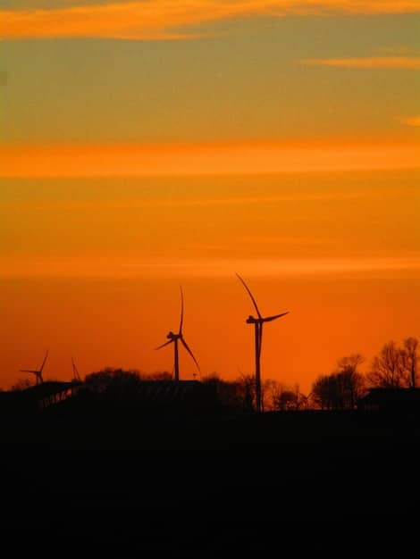 A wind farm at sunset, with large turbines silhouetted against the sky, symbolizing the growing investment in renewable energy sources.