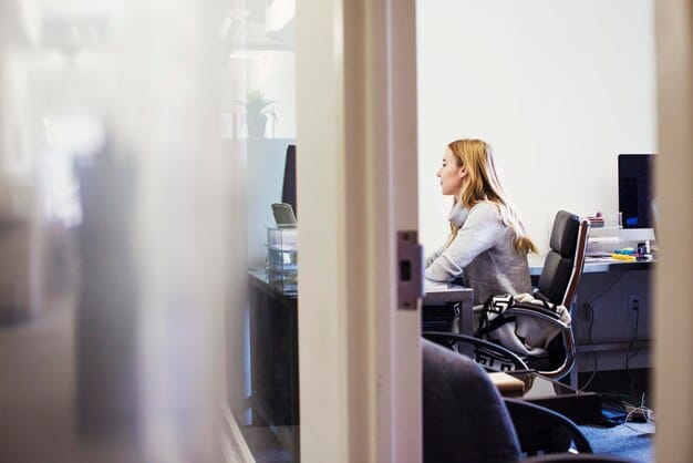 A person in a wheelchair using a computer in a modern, accessible office. The office space is bright and open, with adjustable desks and ergonomic chairs.
