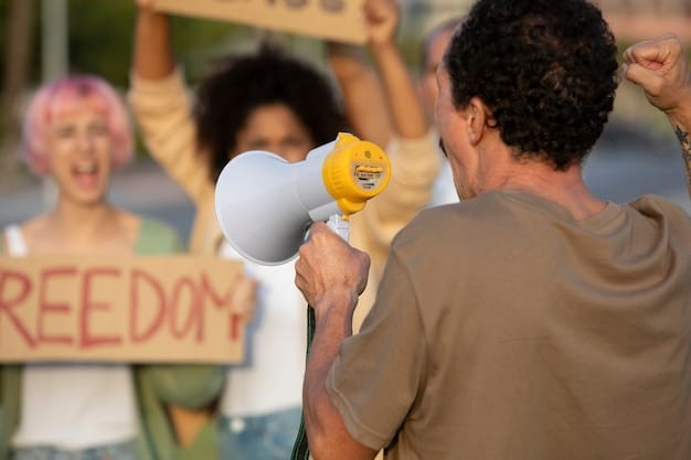 A person holding a megaphone and speaking to a crowd at a community event, while others hold signs and banners.