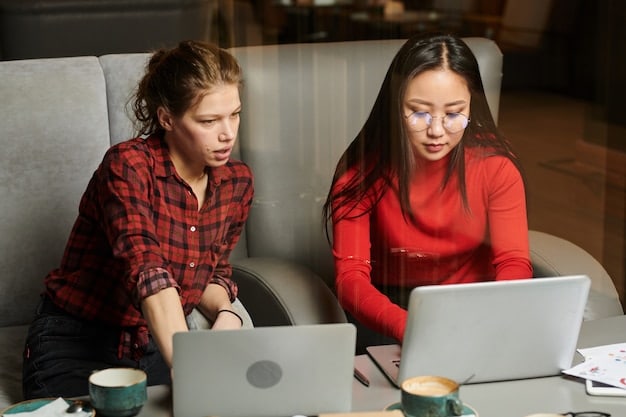 A mentor is sitting at a table with a teen mentee, teaching how to code on a laptop.